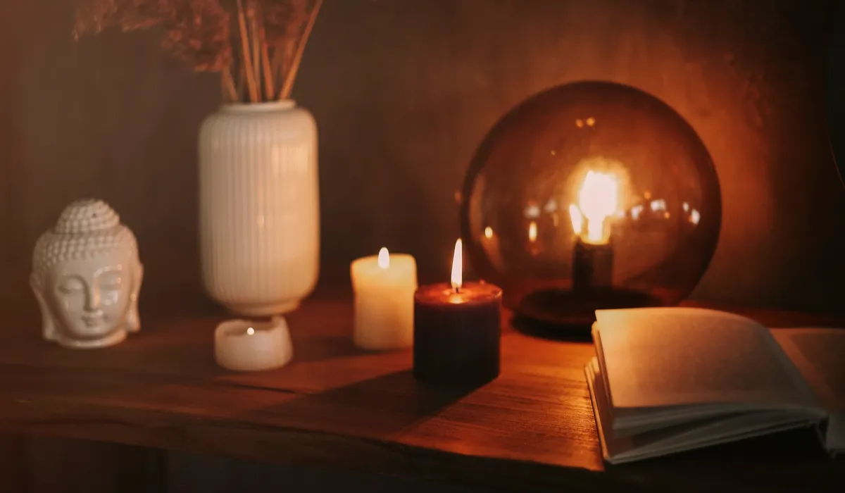 Bodegón con velas encendidas, libro abierto y figura de Buda en cerámica blanca, atmósfera cálida y reflexiva