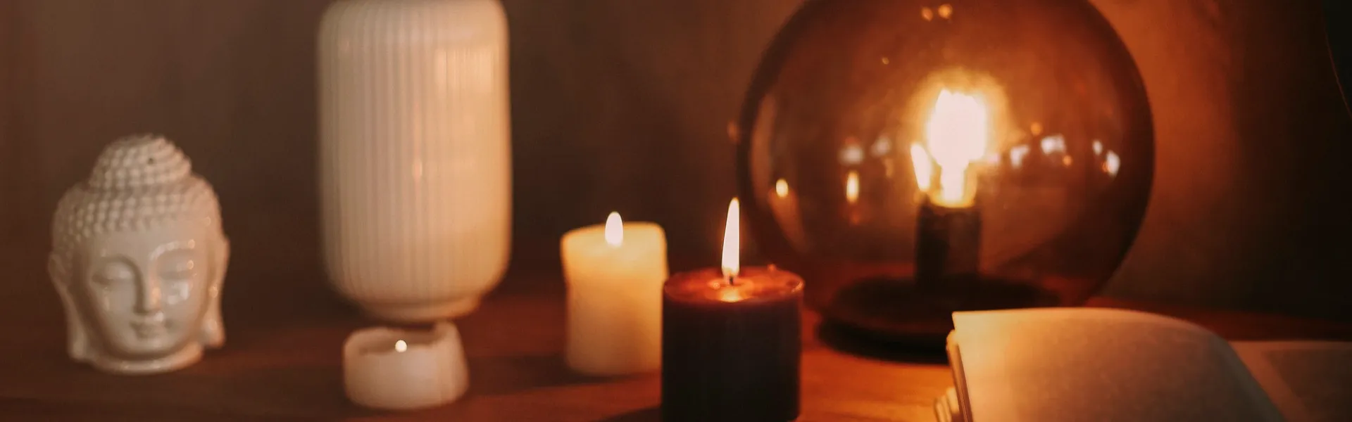 Bodegón con velas encendidas, libro abierto y figura de Buda en cerámica blanca, atmósfera cálida y reflexiva