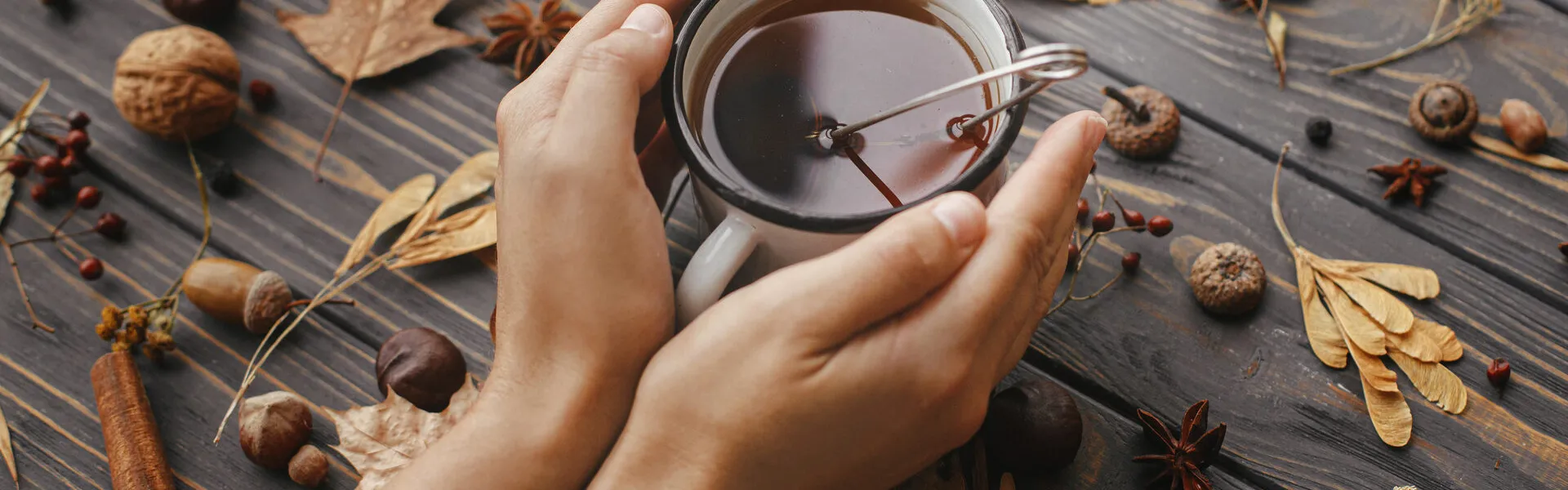 Manos en reposo sobre una mesa de madera clara, junto a una taza de té y un cuaderno abierto, con luz natural suave