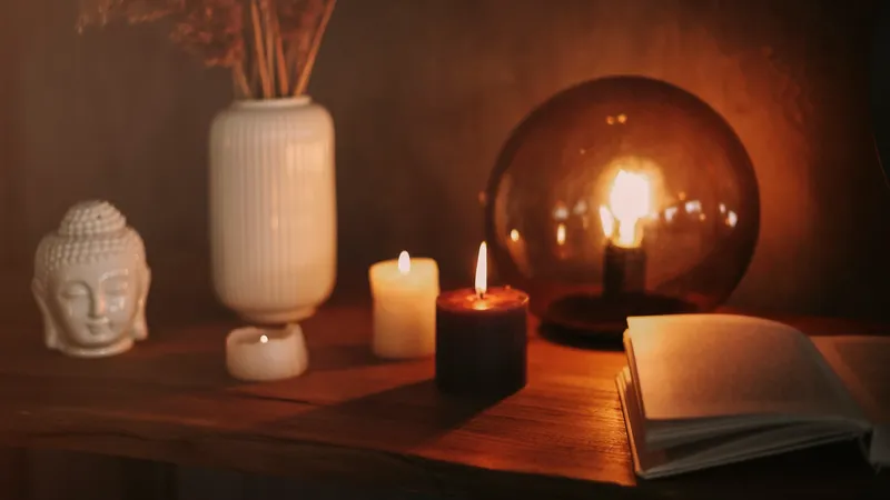 Bodegón con velas encendidas, libro abierto y figura de Buda en cerámica blanca, atmósfera cálida y reflexiva