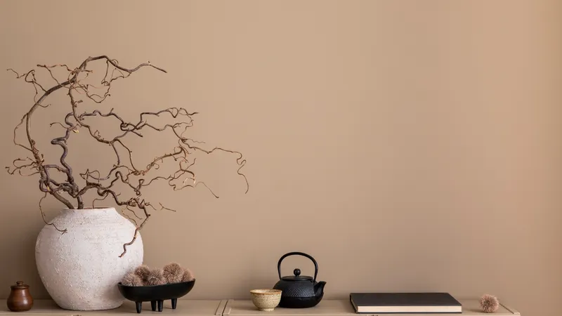Bodegón sereno con vasija de cerámica blanca, ramas secas, tetera japonesa de hierro fundido, taza y libro sobre superficie clara