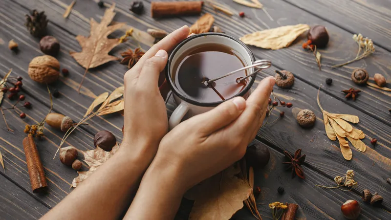 Manos en reposo sobre una mesa de madera clara, junto a una taza de té y un cuaderno abierto, con luz natural suave